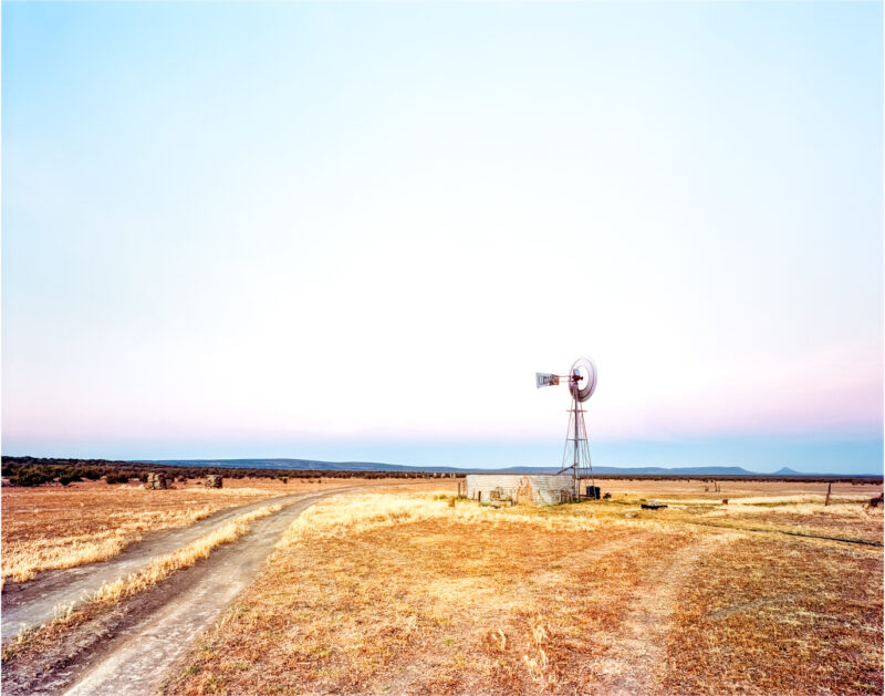Beneath Celestial Fire, a windmill and road beneath a pastel sunset over the Sutherland Plains in South Africa.