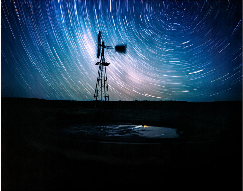 Stillness in Orbit, star trails circling above a windmill and sheep trough on the Sutherland Plains in South Africa.