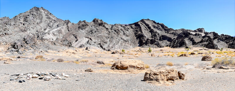 A Dry and Thirsty Land. Panoramic view of stark grey Richtersveld mountains, layered desert rocks and sparse vegetation beside the Orange River in Namibia